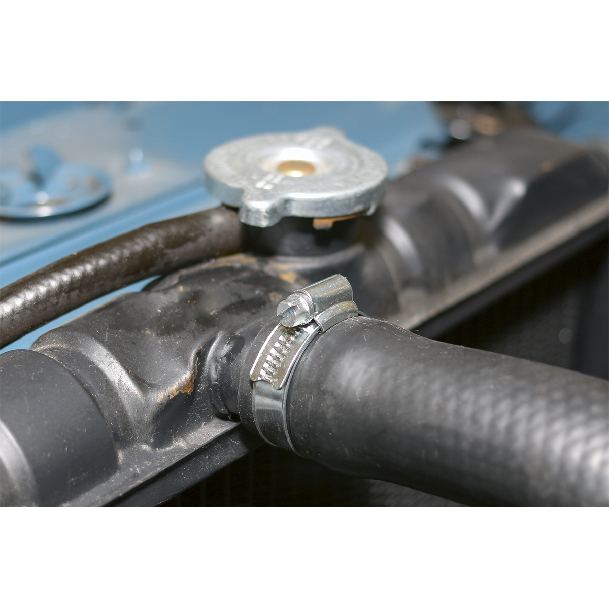 Close-up of a car engine's radiator hose secured with a Sealey HI-GRIP® Hose Clip Zinc Plated Ø50-70mm from the HCJ3 pack of 10, near the radiator cap.