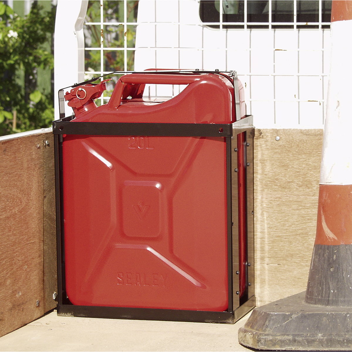 A Sealey Vehicle Bracket for JC20, JC20B, JC20G - JC20VB secures a red 20L jerry can on the back of a vehicle, next to a traffic cone and a metal mesh divider.