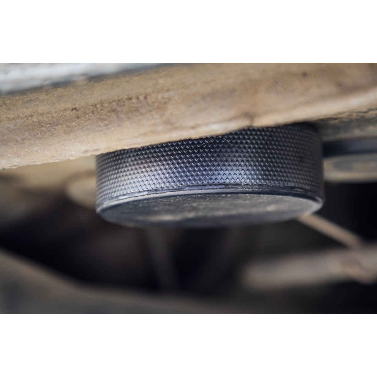 Close-up view of the Sealey Jacking Pad Set Tesla - JPT4, a textured, circular metal object positioned between two wooden surfaces, ensuring a secure fit.