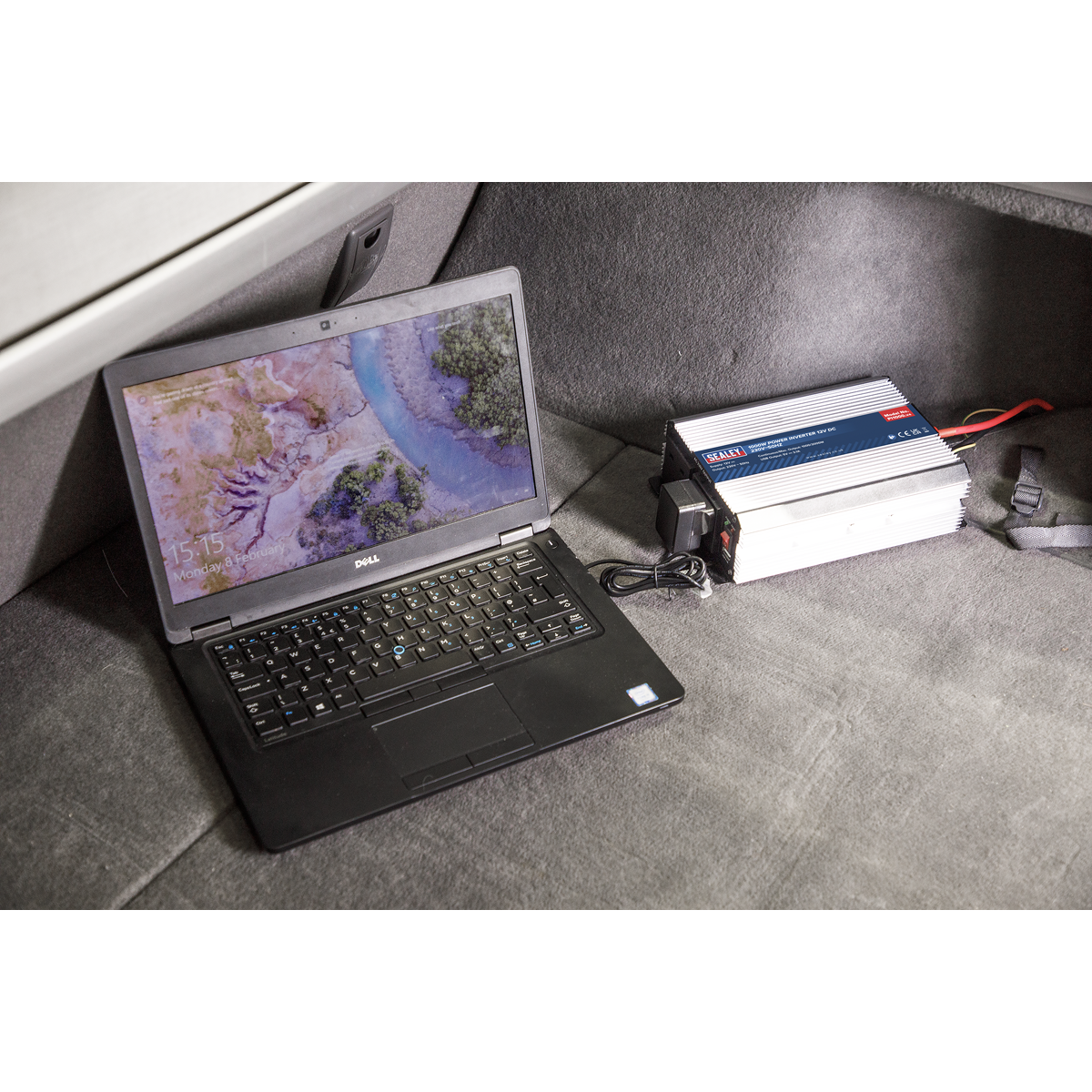 A Dell laptop with a nature-themed desktop is placed on a gray carpeted surface next to a Sealey Power Inverter 1000W 12V DC - 230V~50Hz (PI1000). The setup ensures your device stays powered, utilizing the efficiency and versatility of USB ports for added connectivity.