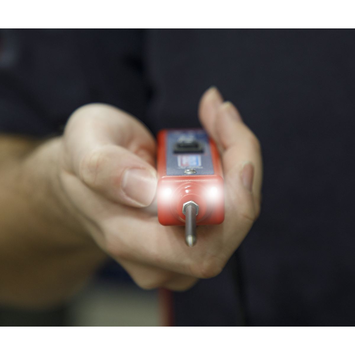 Close-up of a person holding a Sealey Auto Probe Plus 6-24V - PPX with a glowing light at the tip, pointing it forward, against a dark background.