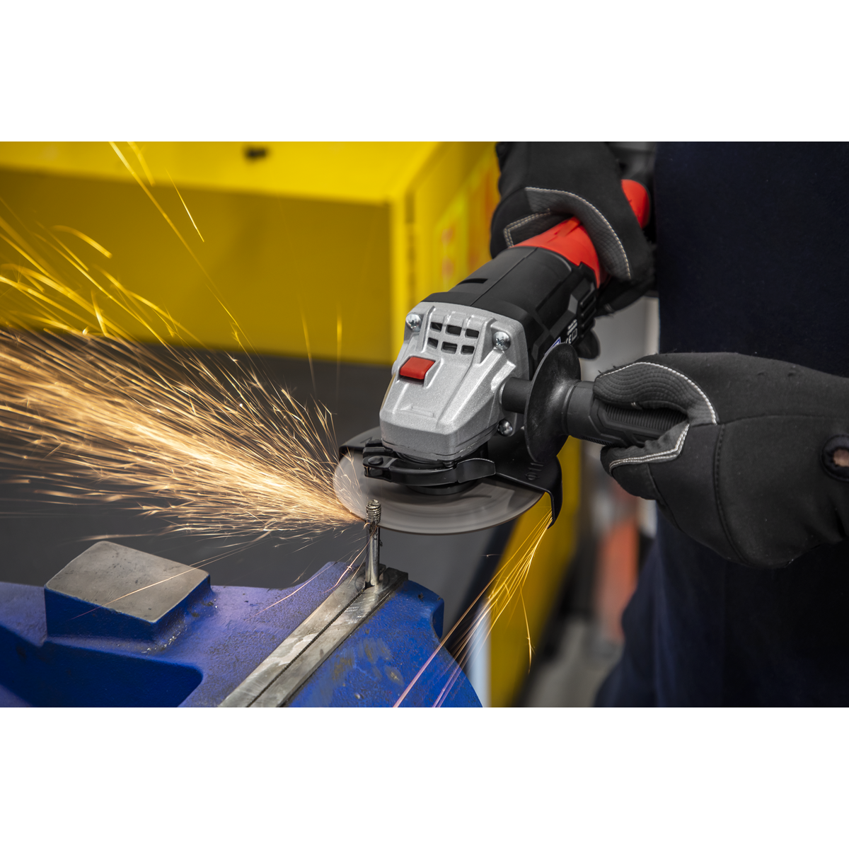 A person using a Sealey Cutting Disc Ø115 x 1.2mm Ø22mm Bore - PTC/115CET to cut stainless steel with an angle grinder, with sparks flying from the cutting area. The metal piece is clamped in a blue vise.