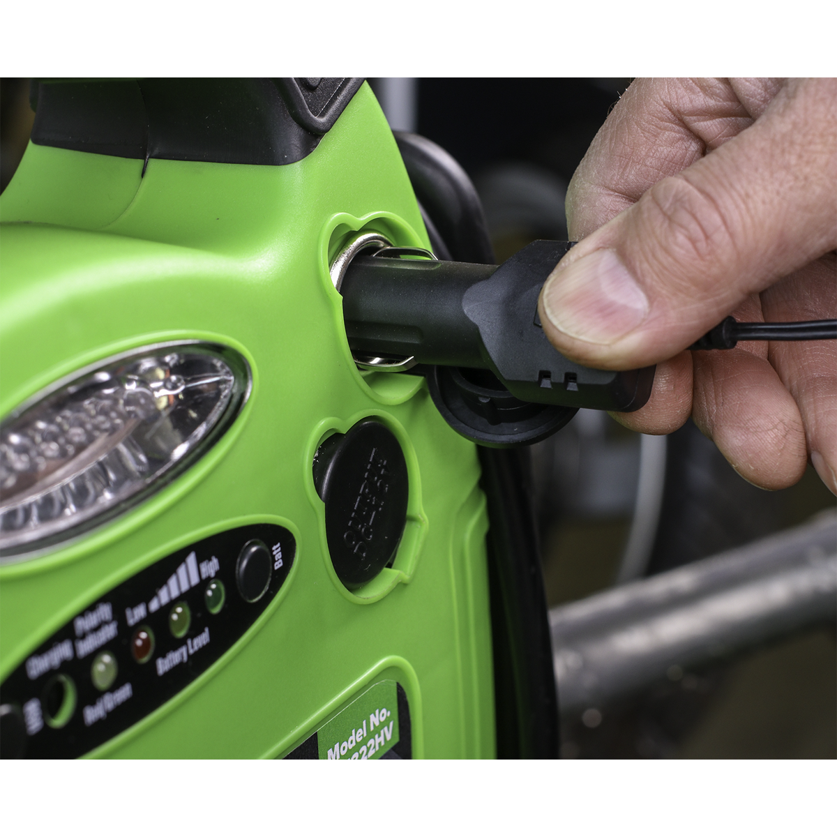 A close-up of a hand inserting a plug into a socket of the Sealey RoadStart® Emergency Jump Starter with Air Compressor 12V 900 Peak Amps - RS1322HV, a green device equipped with various buttons, indicators, and an integral air compressor.