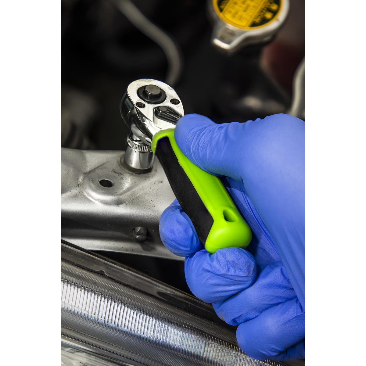 A person wearing blue gloves uses a green and black ratchet wrench from the Sealey Socket Set 25pc 1/4"Sq Drive - Metric - S01233 to work on an automotive component.