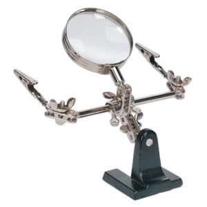 The Sealey Mini Robot Soldering Stand with Magnifier - SD150 features a magnifying glass, adjustable arms, and crocodile clamps mounted on a sleek black stand.