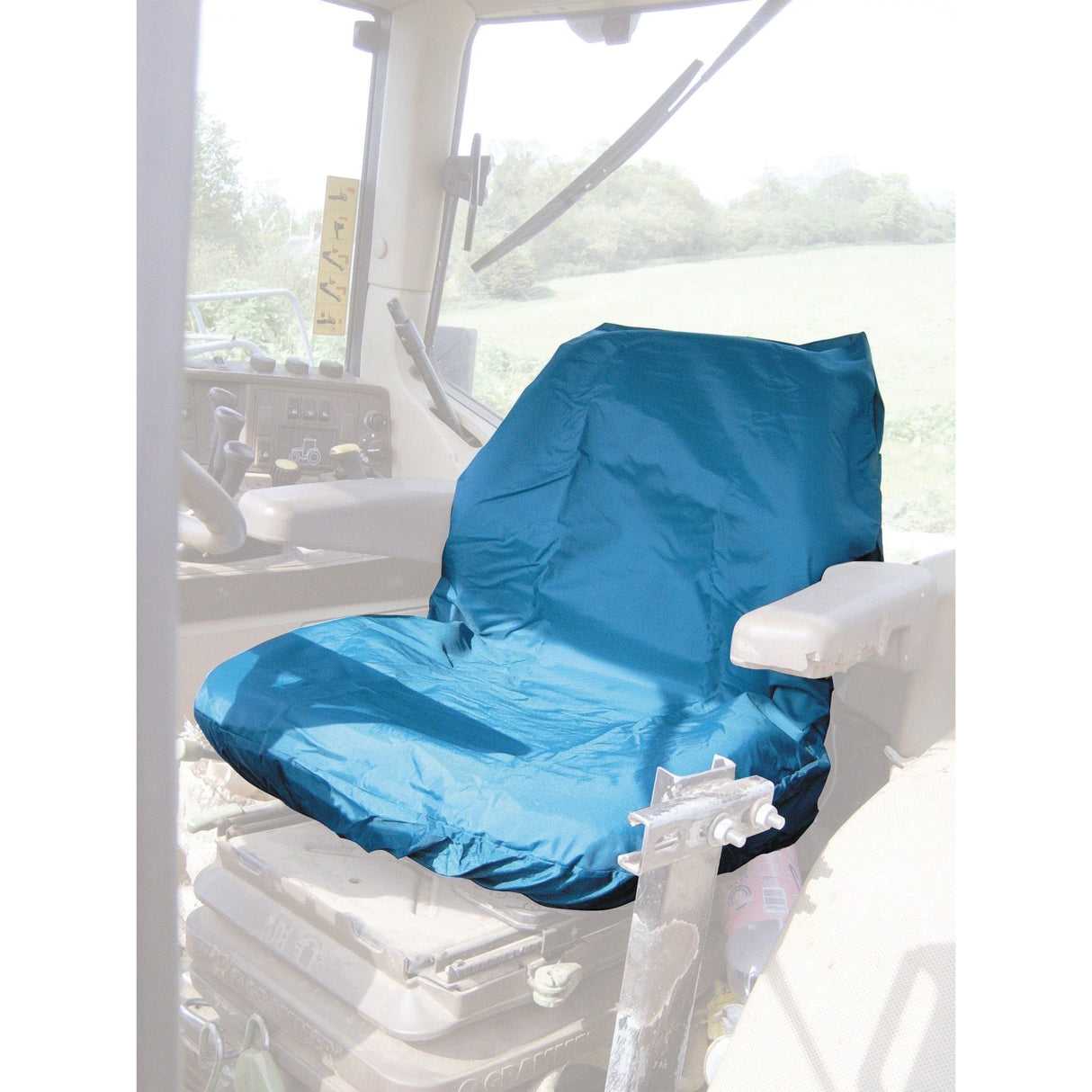 A blue Sparex Standard Seat Cover (S.71716) is installed on a driver's seat inside a vehicle, with a window view of the grassy field outside. It's perfect for a tractor seat and easy to install.