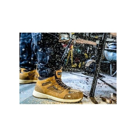 A person wearing JMCE's *SPECIAL PRICE* Buckler Largo Bay Safety Trainers with composite toe caps and dark jeans, working in a workshop with sawdust flying around.