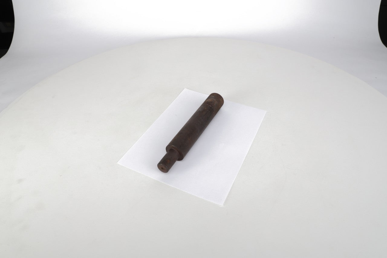 A rusted metal cylindrical object rests on a white sheet of paper against a plain white background, reminiscent of the rugged durability seen in vintage tools like the AGCO | Tool - Act0002680.