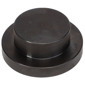 The AGCO Seal Kit - Acp0437710 is a round, black metallic disc featuring a raised circular section in the center, resembling a large button or cap.