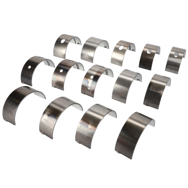 A set of fourteen curved metal engine bearings with holes and slots arranged in rows, compatible with Massey Ferguson tractors. Available as the AGCO Kit, Bearing - 4226952M91 by AGCO.