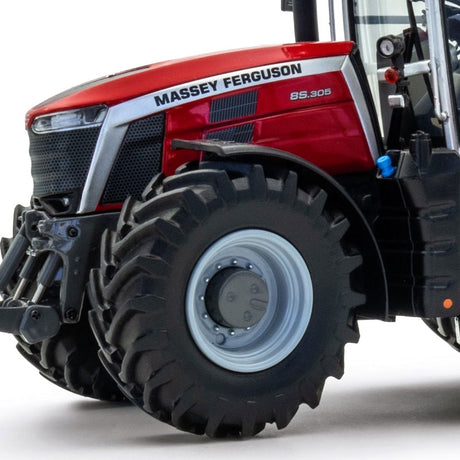 Close-up view of the front section of the Limited Edition Massey Ferguson 8S.305 tractor by JMCE DEALS, highlighting the light gray rims on the front tire and part of the cab with its clear cabin windows.