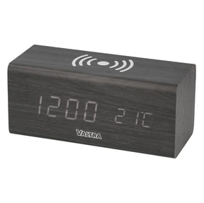 A rectangular digital clock with a black woodgrain finish displaying the time "12:00" and temperature "21°C." The top surface has a wireless charging symbol. The USB-powered alarm clock, named Wireless Charger/Alarm Clock - V42806110, features the brand name "AGCO" below the LED display.