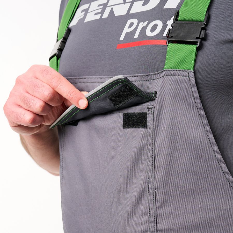 Close-up of a person wearing gray Fendi Professional overalls with green suspenders and a hand pulling open a front pocket.
