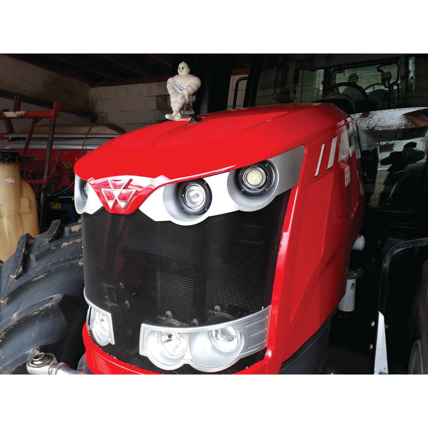 A red tractor with a figure of the Michelin Man on its hood is parked in a garage, illuminated by a Sparex LED Work Light (Cree High Power) boasting 3,000 lumens and 5700K brightness. Various equipment is visible in the background, highlighting the tractor's IP68 rating durability against dust and water.