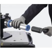 A person wearing gloves is holding the NTN SNR IFT SET 33 Bearing Mounting Kit - S.153978 from Sparex with one hand and a mallet with the other, near a machinery setup with impact rings.