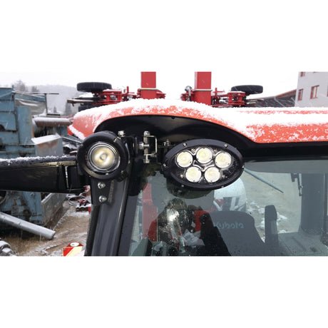 Close-up of a red tractor roof featuring Thomas LED work lights, antennas, and some snow accumulation. In the background, there is industrial equipment and a building. The tractor uses an Adapter suitable for S.150527 & S.150528 LH from Sparex (Part No.S.154014).