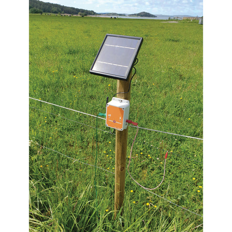 A Sparex Fence Alarm - Luda (S.156395) solar panel and electric fence controller, enhanced with the FenceAlarm app, mounted on a wooden post in a grassy field.