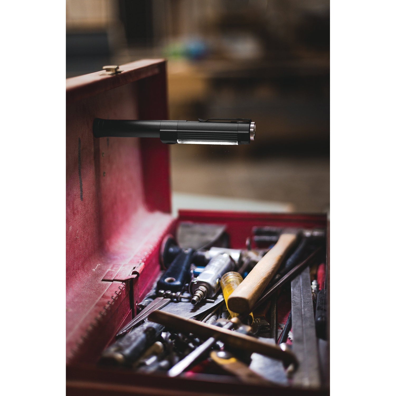 An open toolbox filled with various tools such as hammers, screwdrivers, and pliers. A Sparex Nebo BIG LARRY 2 LED Light - S.162676 with a magnetic base is attached to the interior of the lid, illuminating the tools inside.