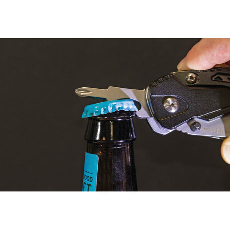 The True Utility HANDYMAN - S.162680 by Sparex, an ergonomic multi-tool with a skeleton-style frame, is being used to open a bottle with a blue cap against a dark background.