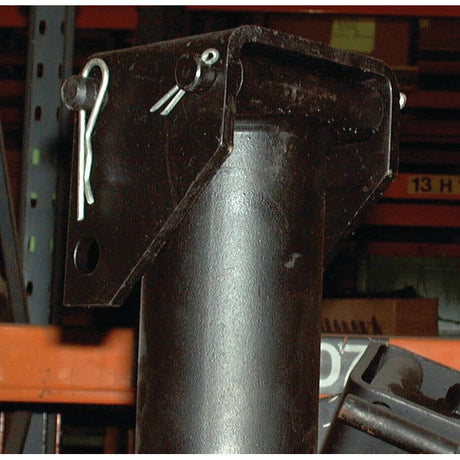 Close-up of the PARKING JACK-5T HYDRAULIC - S.2338 by Sparex, featuring its steel bracket and cylindrical post secured with a pin and clip, with shelves and boxes visible in the background.