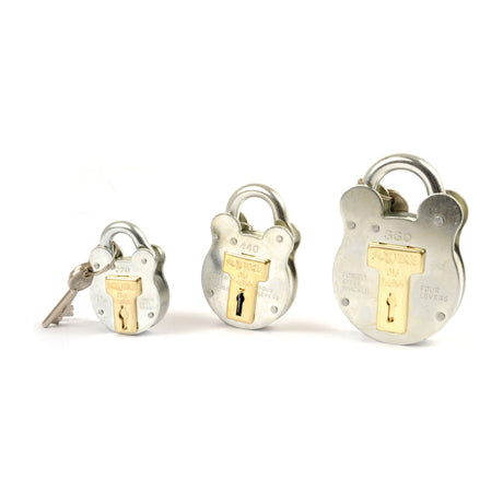 Three Squire Old English Padlocks in silver, distributed by Sparex, are lined up in a row with a key beside the smallest padlock on the left. These steel padlocks, each with a 64mm body width and a security rating of 3, exhibit brand markings and brass keyholes, crafted to withstand outdoor conditions and harsh environments.