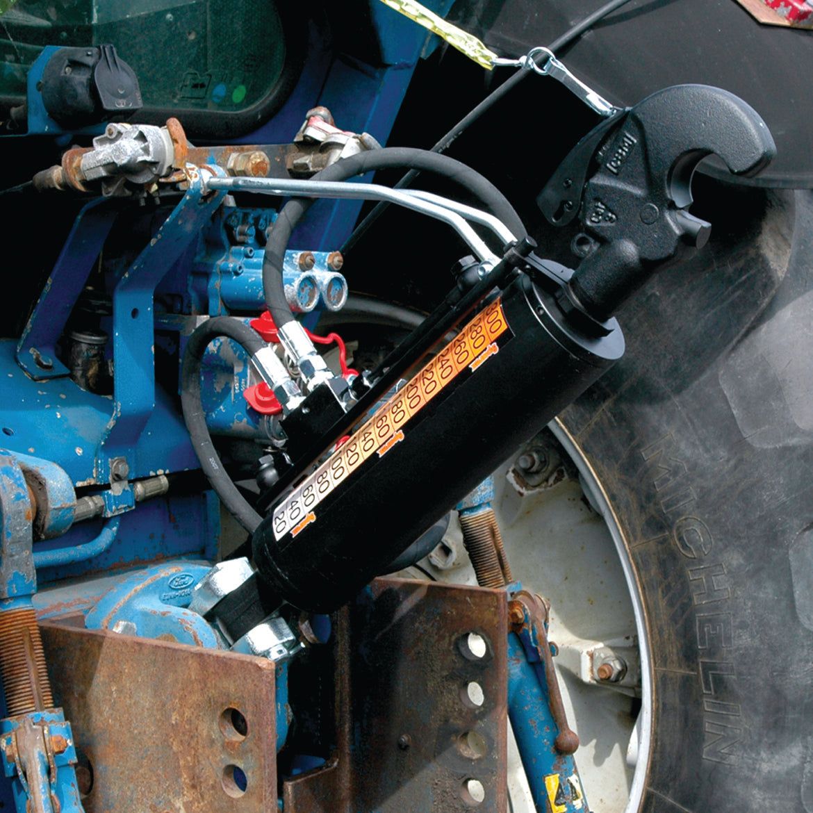 Close-up of a Sparex Hydraulic Top Link (Cat.3/3) Knuckle and Q.R CBM Hook with a 90mm cylinder bore and a minimum length of 650mm, mounted on a blue tractor behind the vehicle tire. (Sparex Part No.S.331201)