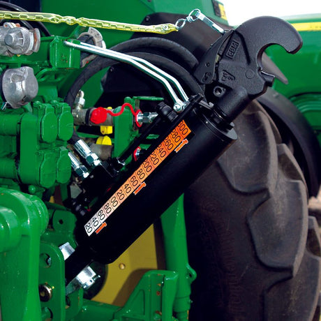 Close-up of the Claas ARION tractor highlighting Sparex's Hydraulic Top Link (Cat.2/3) Knuckle and Q.R CBM Hook, featuring a 90mm cylinder bore and a minimum length of 650mm. The setup showcases hydraulic machinery with black and green components attached to the vehicle, along with various pipes, a chain, and red, black, and silver parts against the backdrop of a large wheel. A prominent Sparex hydraulic cylinder is prominently featured in the assembly.