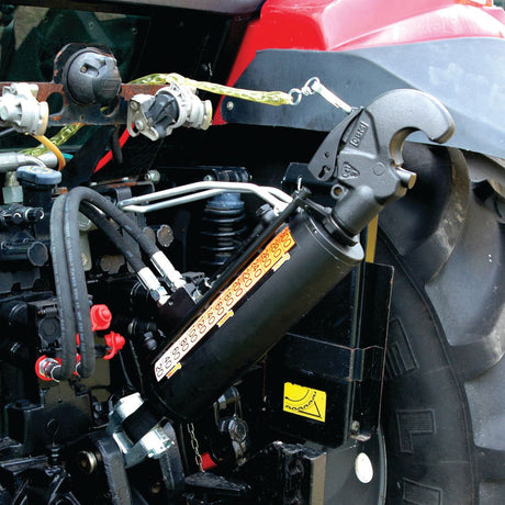 Close-up of the Sparex Hydraulic Top Link (Cat.36mm/3) Knuckle and Q.R CBM Hook, Cylinder Bore: 90mm, Min. Length: 650mm (Sparex Part No.S.331204) on a red agricultural tractor. Various cables and connections are visible, and there are labels on the hydraulic cylinder.