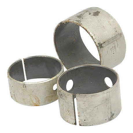 Three worn cylindrical metal sleeves from a Sparex Camshaft Bush Kit (Engine Model - S.57369, ID: Semi Finished mm), with visible scratches and holes, arranged in a scattered manner against a plain background.