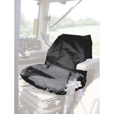 A Sparex Standard Seat Cover - Tractor & Plant - Universal Fit (S.71717) adorns the driver's cabin seat, its black, waterproof material perfectly complementing the view of the green landscape outside the window. This washable cover ensures both comfort and practicality for any journey.