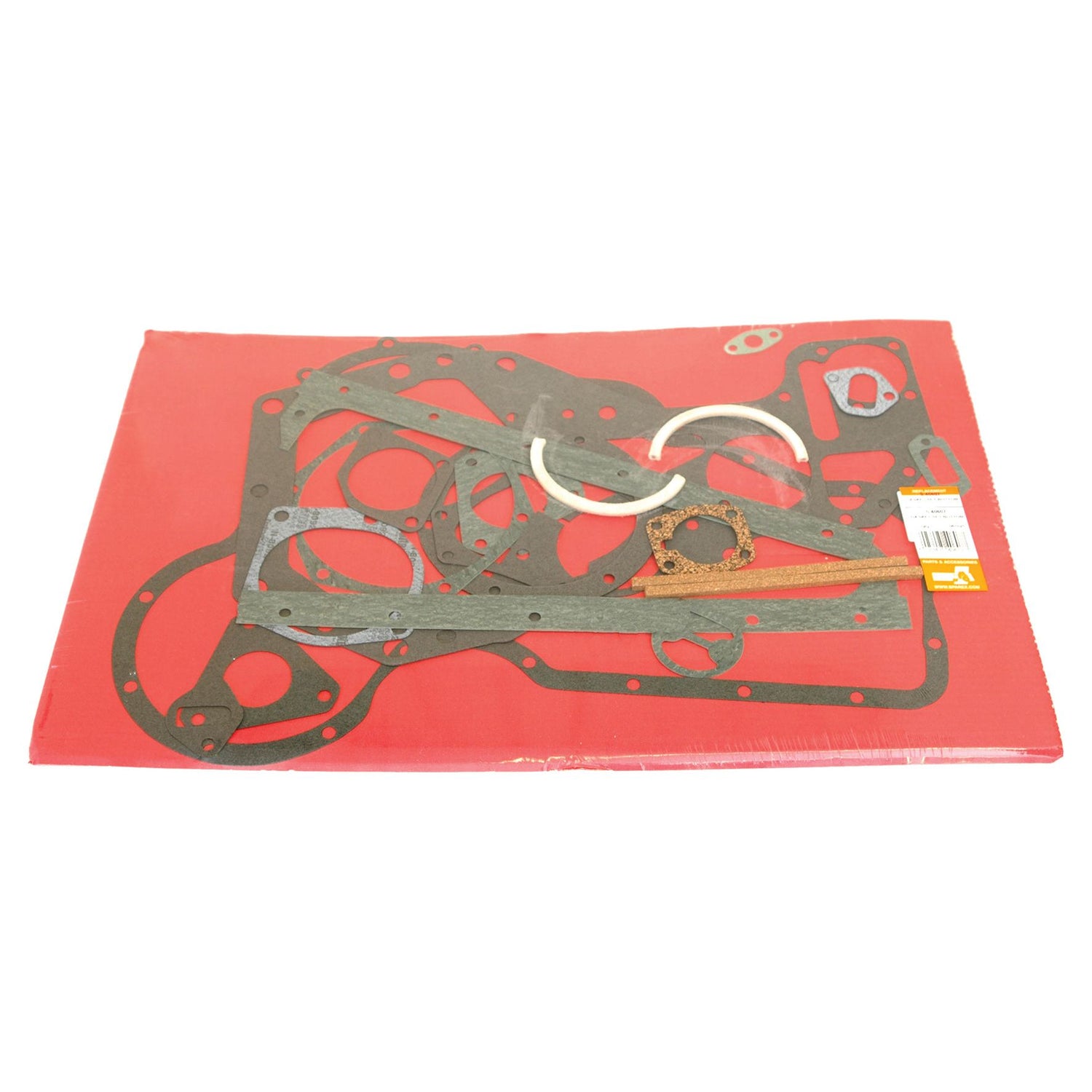 A display of the Bottom Gasket Set - 4 Cyl. (Sparex Part No.S.40607) by Sparex is showcased on a red surface, featuring an assortment of various shapes and sizes designed to seal engine components for Perkins and Massey Ferguson types.