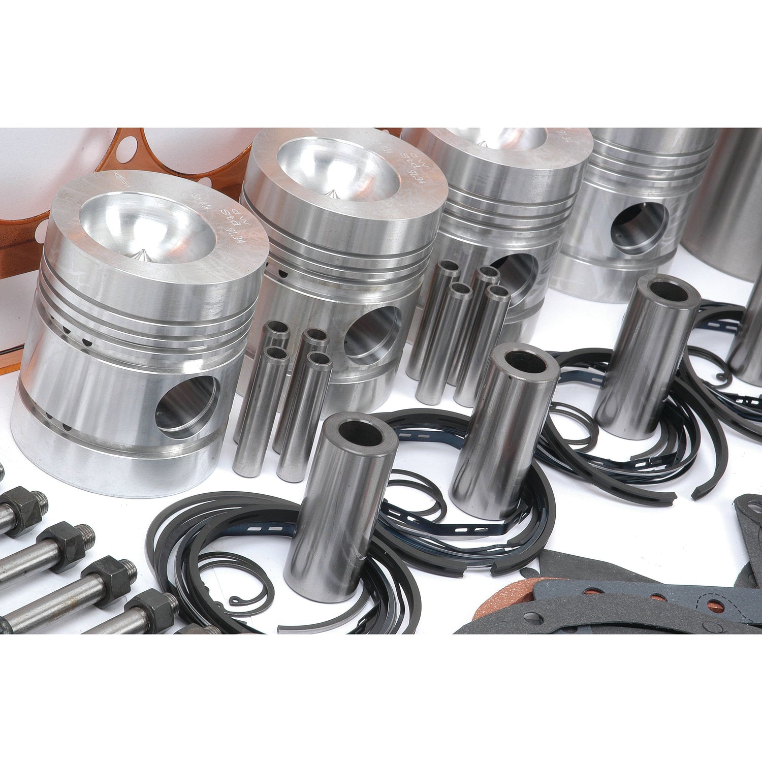 Close-up of Sparex Perkins Engine components, including pistons, piston rings, and various cylindrical parts, arranged neatly on a white surface as part of the Engine Overhaul Kit with Valve Train (Finished) - S.41601.