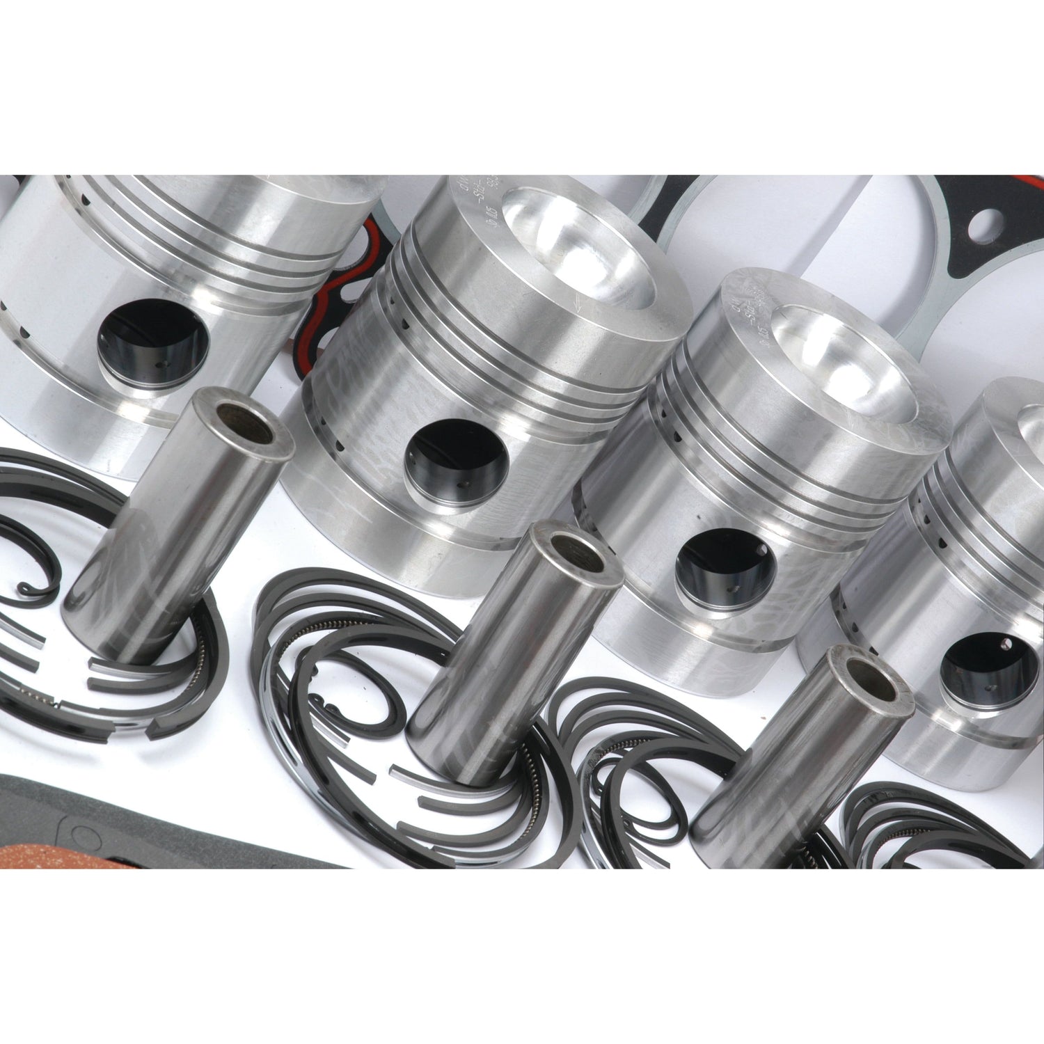 Four silver engine pistons with accompanying rings and components, arranged on a white surface, form a crucial part of the Engine Overhaul Kit without Valve Train (Finished) by Sparex, suitable for Perkins Engine Model in Landini Massey Ferguson tractors. Sparex Part No. S.41907.