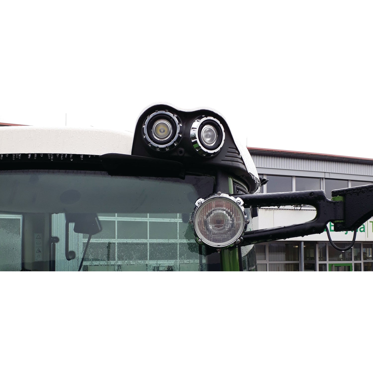 Close-up of a tractor's headlight assembly featuring two round LED Work Lights (Cree High Power) by Sparex, and a side mirror, with a building visible in the background. The setup includes an integrated 2 pin Deutsch connector, ensuring reliable performance even in harsh conditions thanks to its IP68 rating. Each light delivers 3000 lumens of raw power and operates within a voltage range of 10-36V, meeting Class 3 interference standards (S.153707).