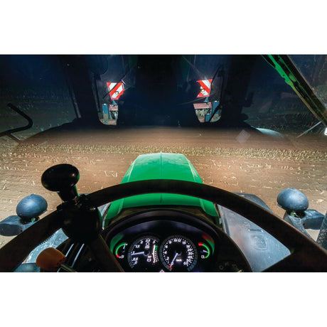 View from inside a tractor at night, featuring the illuminated dashboard and the field ahead through the front windshield. The scene is well-lit by the Sparex LED Work Light (Cree High Power), emitting 7000 lumens. This powerful Class 3 light ensures that suitable information is displayed for navigating and operating effectively in low-light conditions, with a voltage range of 10-60V (S.130024).