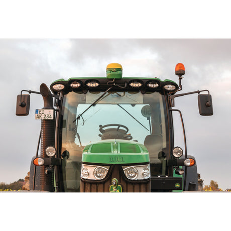 Front view of a green agricultural tractor equipped with Sparex LED Work Lights (Cree High Power, 7000 Lumens Raw, 10-60V - S.130024) and various mirrors, featuring a license plate labeled “AK 234.” Suitable for diverse farming activities, the tractor stands against an overcast sky.