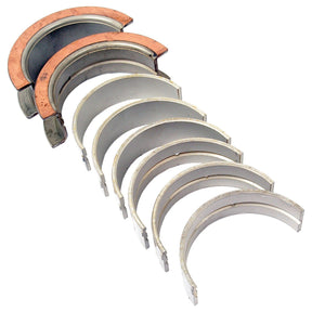 A set of eight beige semi-circular main bearings, including two with copper-colored inner surfaces, arranged in a row and compatible with Ford/New Holland vehicles. This product is sold by Sparex and is listed under part number S.65219 as "Main Bearing +0.010'' (0.25mm) (Set).