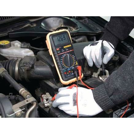 A person wearing gloves uses the Sparex Multimeter - S.151761 for voltage measurement in a car engine compartment, showcasing typical automotive applications.